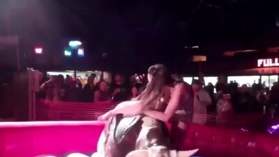 Une jeune fille en robe courte fait un tour sur un taureau mécanique