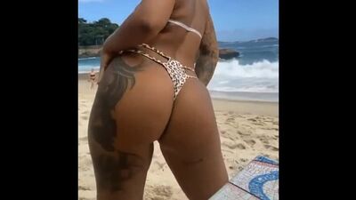 Una morena tatuada con un bikini ajustado en la playa bailando funk